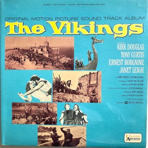 Puede incluir: La portada del álbum de la banda sonora original de la película "Los Vikingos" presenta un fondo azul con imágenes de las estrellas de la película Kirk Douglas, Tony Curtis, Ernest Borgnine y Janet Leigh. El título del álbum "The Vikings" está en letras amarillas grandes.