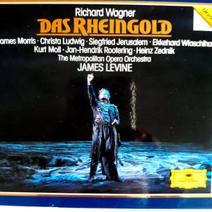 May include: A vintage album cover for Richard Wagner's "Das Rheingold" featuring James Levine and The Metropolitan Opera Orchestra. The cover displays a performance scene with a costumed figure against a dark background, with the album title and artist names prominently displayed.