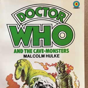 May include: A book cover for the Doctor Who novel "And the Cave-Monsters" by Malcolm Hulke. The cover features a green and black illustration of a dinosaur and a monster with a green, scaly face.