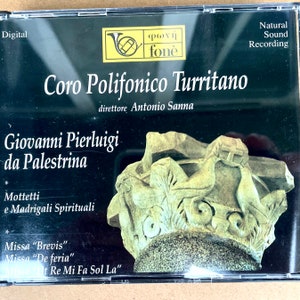 Puede incluir: Una caja de CD con fondo negro y texto blanco. El texto dice "Coro Polifonico Turritano" y "Giovanni Pierluigi da Palestrina". La imagen también incluye una foto de una escultura de piedra con una cruz.