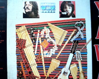 Puede incluir: Una portada de CD titulada El mundo de los Beatles en el Perú con retratos de Ringo Starr y Paul McCartney. Debajo, una colección de instrumentos musicales andinos que incluye flautas de pan, un charango y una guitarra sobre un tejido a rayas.