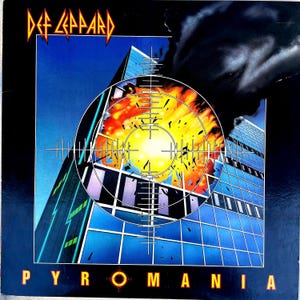 Könnte beinhalten: Albumcover für Def Leppard's Pyromania. Das Artwork zeigt ein Hochhaus, das von einem Fadenkreuz anvisiert wird, mit einer Explosion in der Mitte. Der Name der Band steht oben und der Albumtitel unten.