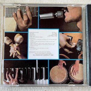 May include: A CD case back insert featuring a collage of musical scenes including a guitar fretboard, a person singing into a microphone, maracas, a guitar body, piano keys, and conga drums, with printed track lists and credits for Kalapana.