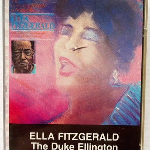 Puede incluir: Una cinta de casete con Ella Fitzgerald cantando The Duke Ellington Songbook. La portada presenta un retrato colorido de Ella Fitzgerald con un fondo rosa y azul.
