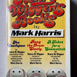 Puede incluir: Portada de libro con fondo amarillo y el título "Henry Wiggen's Books" en letras rojas y naranjas. El nombre del autor, "Mark Harris", está impreso en negro debajo del título. La portada también presenta tres pelotas de béisbol con caras, cada una representando un libro diferente de Henry W. Wiggen: "The Southpaw", "Bang the Drum Slowly" y "A Ticket for a Seamstitch".