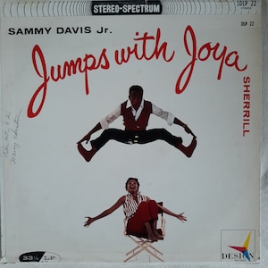 May include: A vintage vinyl record album cover featuring Sammy Davis Jr. jumping in the air with a joyful expression. The album title is "Jumps with Joya" and the record label is "Sherrill".