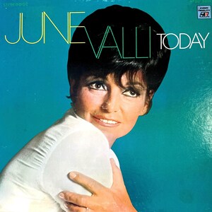 Puede incluir: Portada del álbum "Today" de June Valli. La carátula presenta a una mujer con cabello oscuro y una blusa blanca sobre un fondo turquesa. El texto "JUNE VALLI" está en una fuente estilizada, con "TODAY" en una fuente blanca limpia.