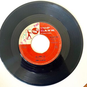 May include: A red and white vinyl record with the text "Top Rank International" and "45-JAR-269" on the label. The record is titled "Go, Jimmy, Go" by Jimmy Clanton.