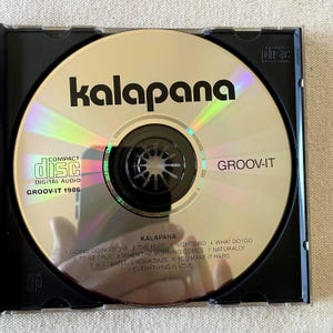 May include: A silver compact disc titled Groov-It by Kalapana, released in 1986. The disc features the band name, album title, and a tracklist including Going Going Gone, The Hurt, Nightbird, What Do I Do, To Be True, When The Morning Comes, Naturally, All I Want, Kona Daze, You Make It Hard, and Everything Is Love.