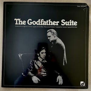 Puede incluir: Portada de álbum negra para "The Godfather Suite" con una imagen en blanco y negro de dos hombres. El título está en letras blancas grandes, con los nombres del director, la orquesta y los compositores debajo.