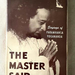 Może przedstawiać: Okładka książki z portretem mężczyzny ze splecionymi dłońmi. Tytuł "THE MASTER SAID..." jest wyraźnie widoczny, a także nazwisko autora i "Sayings of PARAMHANSA YOGANANDA". Książka ma niebieski grzbiet.