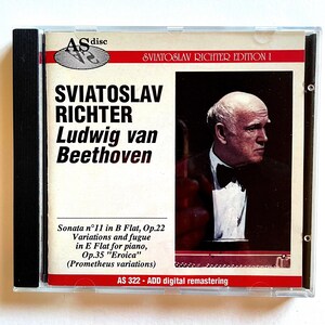 May include: A CD case with a black spine and a colourful front cover. The cover features a photo of a man in a tuxedo, with the text "Sviatoslav Richter Edition I" and "Sviatoslav Richter Ludwig van Beethoven" in large, bold font. The text "Sonata nº11 in B Flat, Op.22 Variations and fugue in E Flat for piano, Op.35 "Eroica" (Prometheus variations)" is printed in smaller font below the photo. The text "AS 322 - ADD digital remastering" is printed in the bottom right corner.