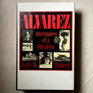 May include: A hardcover book titled "ALVAREZ Adventures of a Physicist." The cover features a black and red design with the title in large red letters. It includes several black and white images, including a portrait and a mushroom cloud.