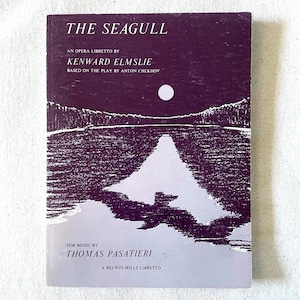 May include: A vintage book cover for "The Seagull" opera libretto. The cover features a dark purple background with a white illustration of a lake scene under a full moon. Text includes the title, author, and composer.