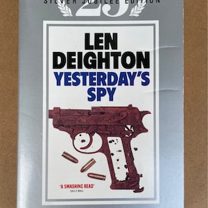 May include: A book cover for "Yesterday's Spy" by Len Deighton. The cover is silver with the text "Silver Jubilee Edition" at the top. The title is in large black and blue letters, with a rusty gun illustration and bullets.