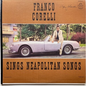 May include: A vintage record album cover featuring Franco Corelli, a man in a light-colored suit standing next to a silver convertible car. The album title is "Franco Corelli Sings Neapolitan Songs".