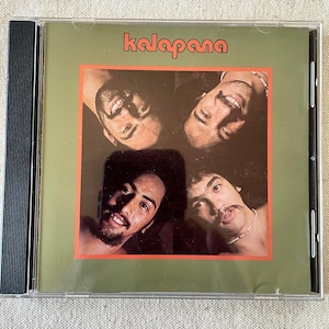 May include: A compact disc case featuring a green cover with the word kalapana printed in orange at the top. The center square contains a photograph of four individuals arranged in a grid, all smiling and looking toward the camera lens.