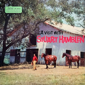 Pode incluir: Uma capa de álbum de vinil vintage com um homem de camisa vermelha e calças marrons em pé na frente de um celeiro branco com dois cavalos marrons. O título do álbum é "A Visit With Stuart Hamblen".