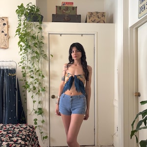 Puede incluir: Una mujer con un top estampado con detalles de plumas azules y shorts vaqueros azul claro. El top presenta un dise&ntilde;o floral amarillo y azul. Los shorts tienen un dise&ntilde;o cl&aacute;sico de cinco bolsillos.