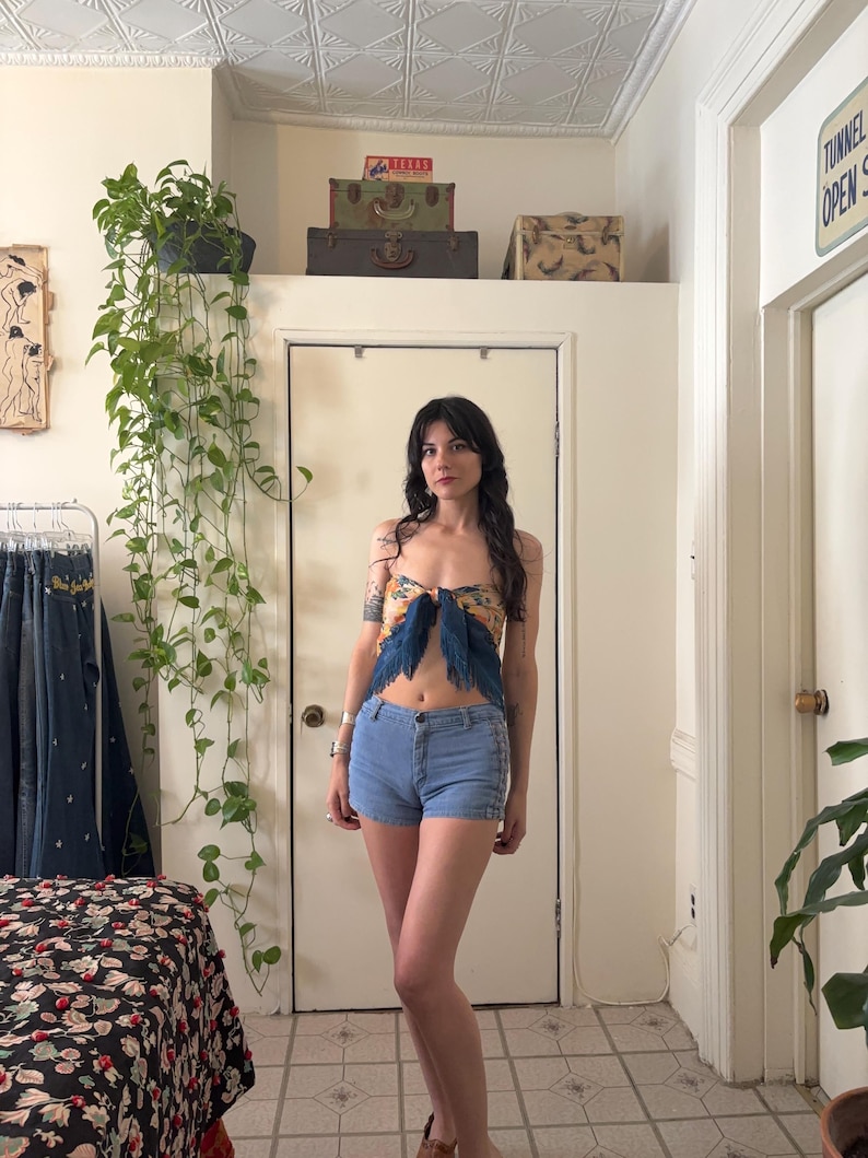 Puede incluir: Una mujer con un top estampado con detalles de plumas azules y shorts vaqueros azul claro. El top presenta un dise&ntilde;o floral amarillo y azul. Los shorts tienen un dise&ntilde;o cl&aacute;sico de cinco bolsillos.