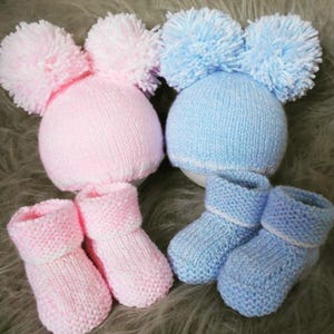 May include: Two sets of knitted baby booties and hats. One set is pink with white pom-poms and the other is blue with white pom-poms.