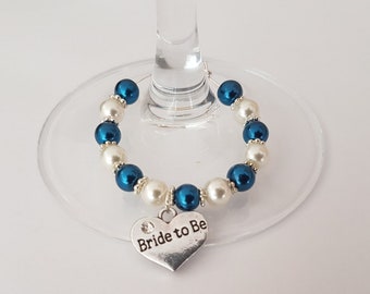 May include: A white and teal blue beaded glass charm with a silver heart charm that says "Bride to Be".