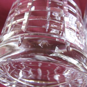 Może przedstawiać: Zbliżenie na przezroczysty, szlifowany kryształowy kieliszek z geometrycznym wzorem. Kieliszek ma grubą podstawę i teksturowaną powierzchnię. Światło odbija się od cięć, tworząc efekt iskrzenia. Kieliszek jest prawdopodobnie częścią zestawu szkła.