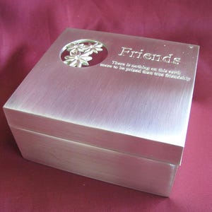 May include: A silver-colored box with the word "Friends" engraved on the lid. The lid features a floral design and an inscription that reads, "There is nothing on this earth more to be prized than true friendship."