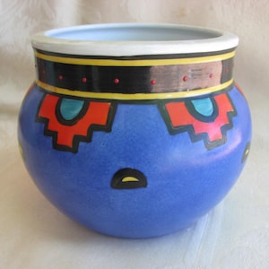 May include: A blue ceramic planter with a geometric design in red, yellow, black, and turquoise. The planter has a white rim and a glossy finish.