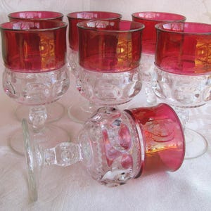 May include: Set of six vintage wine glasses with ruby red rims and clear, textured bowls. One glass is lying on its side. The glasses have a classic, elegant design, perfect for serving wine or other beverages.