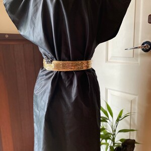 May include: A black sleeveless dress with a gold sequined belt. The dress is made of a smooth, silky fabric.