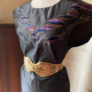 May include: A black dress with a gold sequined belt and a colourful embroidered design on the bodice.