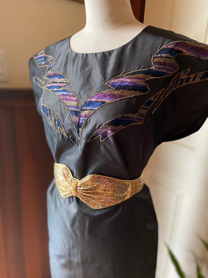 May include: A black dress with a gold sequined belt and a colourful embroidered design on the bodice.