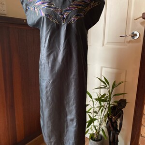 May include: A black sleeveless dress with a geometric pattern embroidered on the neckline. The embroidery is in shades of gold, purple, and blue.