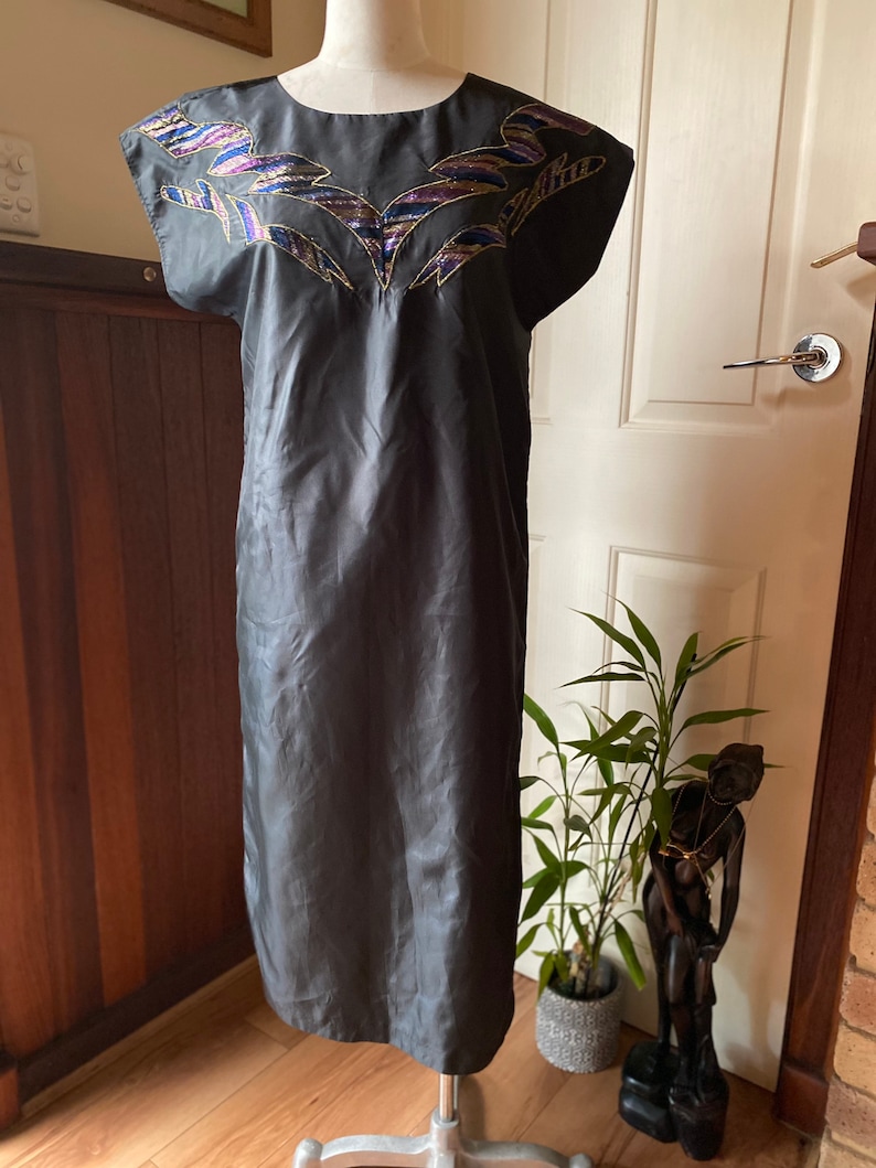May include: A black sleeveless dress with a geometric pattern embroidered on the neckline. The embroidery is in shades of gold, purple, and blue.