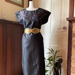 May include: A black sleeveless dress with a gold belt and a colourful embroidered design on the bodice.