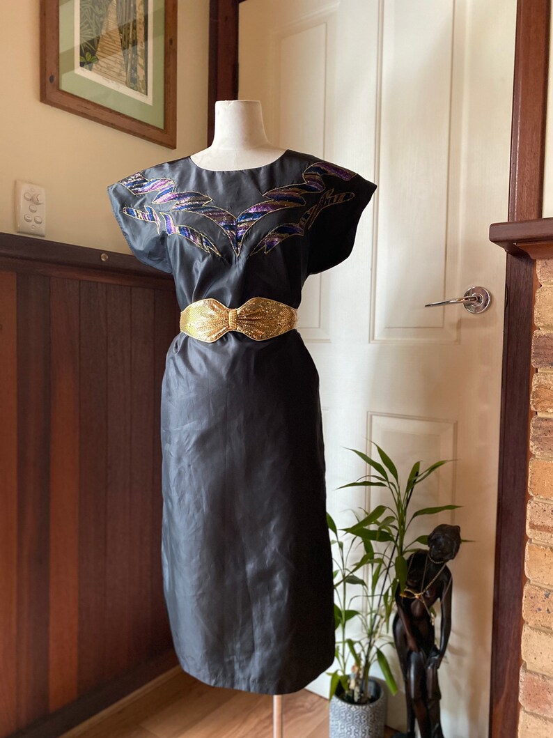 May include: A black sleeveless dress with a gold belt and a colourful embroidered design on the bodice.