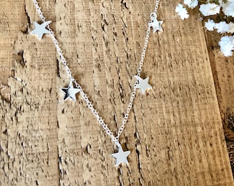 May include: A silver necklace with five star charms hanging from it. The necklace is on a wooden surface.