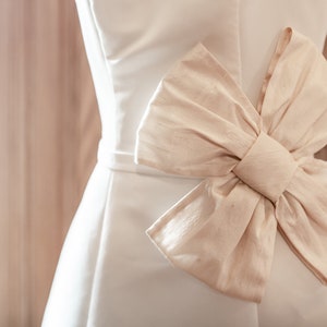 May include: A white satin dress with a large, ivory bow at the waist.