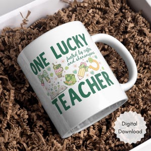 May include: White ceramic mug with the text "ONE LUCKY TEACHER" in green, along with illustrations of a bow, pencil, coffee cup, and a leprechaun hat. The mug is filled with brown packing material.