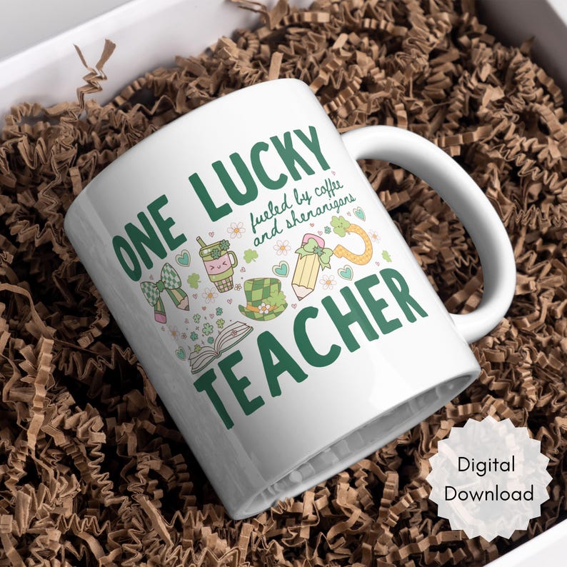 May include: White ceramic mug with the text "ONE LUCKY TEACHER" in green, along with illustrations of a bow, pencil, coffee cup, and a leprechaun hat. The mug is filled with brown packing material.
