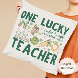 May include: A white pillow with the text "ONE LUCKY TEACHER" in green, along with illustrations of a bow, pencil, coffee cup, hat, and horseshoe. The pillow also has the text "fueled by coffee and shenanigans".