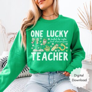 May include: A green sweatshirt with the text "ONE LUCKY TEACHER" in white. The design includes shamrocks, coffee, and other St. Patrick's Day themed graphics. The phrase "fueled by coffee and shenanigans" is also included.