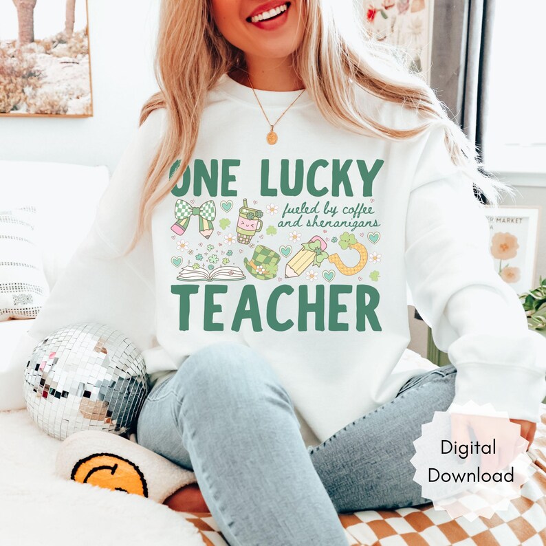 May include: White sweatshirt with the text "ONE LUCKY TEACHER" in green, along with illustrations of a bow, coffee cup, pencil, and shamrock. The phrase "fueled by coffee and shenanigans" is also included.