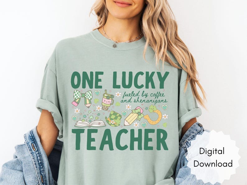 May include: Sage green t-shirt with a St. Patrick's Day theme. The shirt features the text "ONE LUCKY TEACHER" with graphics of a bow, coffee cup, pencil, and shamrock. The phrase "fueled by coffee and shenanigans" is also included.