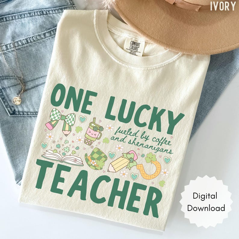 May include: Ivory-colored t-shirt with the text "ONE LUCKY TEACHER" in green, along with illustrations of a bow, pencil, coffee cup, and shamrock. The shirt also includes the phrase "fueled by coffee and shenanigans."