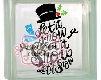 May include: A glass block with a black and white snowman design. The snowman has a black top hat and a red holly sprig. The text "Let it snow Let it snow Let it snow" is written in black.