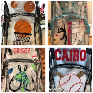 May include: Four clear backpacks with different designs. The first backpack has a basketball and the name "Kraigan" on it. The second backpack has a volleyball player and the name "Mirella" on it. The third backpack has a fishing lure and the name "Griggs" on it. The fourth backpack has a baseball and the name "Cairo" on it.