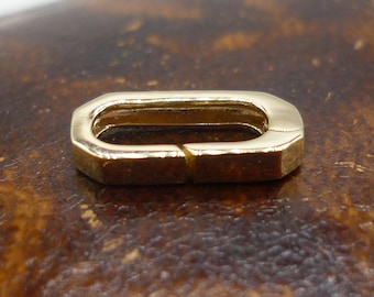 May include: A gold-toned metal connector with a rectangular shape and rounded edges. The connector has a small opening in the center.