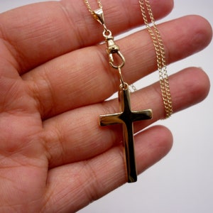 May include: A gold chain necklace with a large gold cross pendant. The chain is a delicate, thin chain and the cross is a simple, flat design.